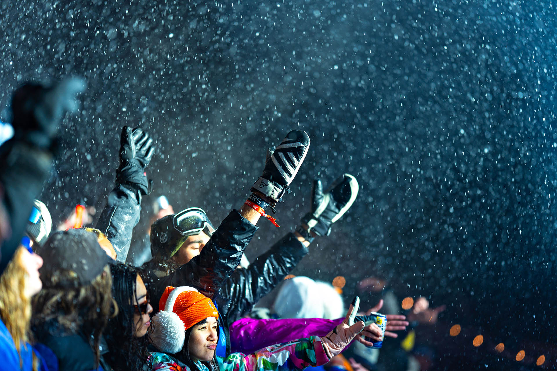 Crowd celebrating in falling snow at Snow Machine Hakuba, with skiers and snowboarders dancing in winter gear.