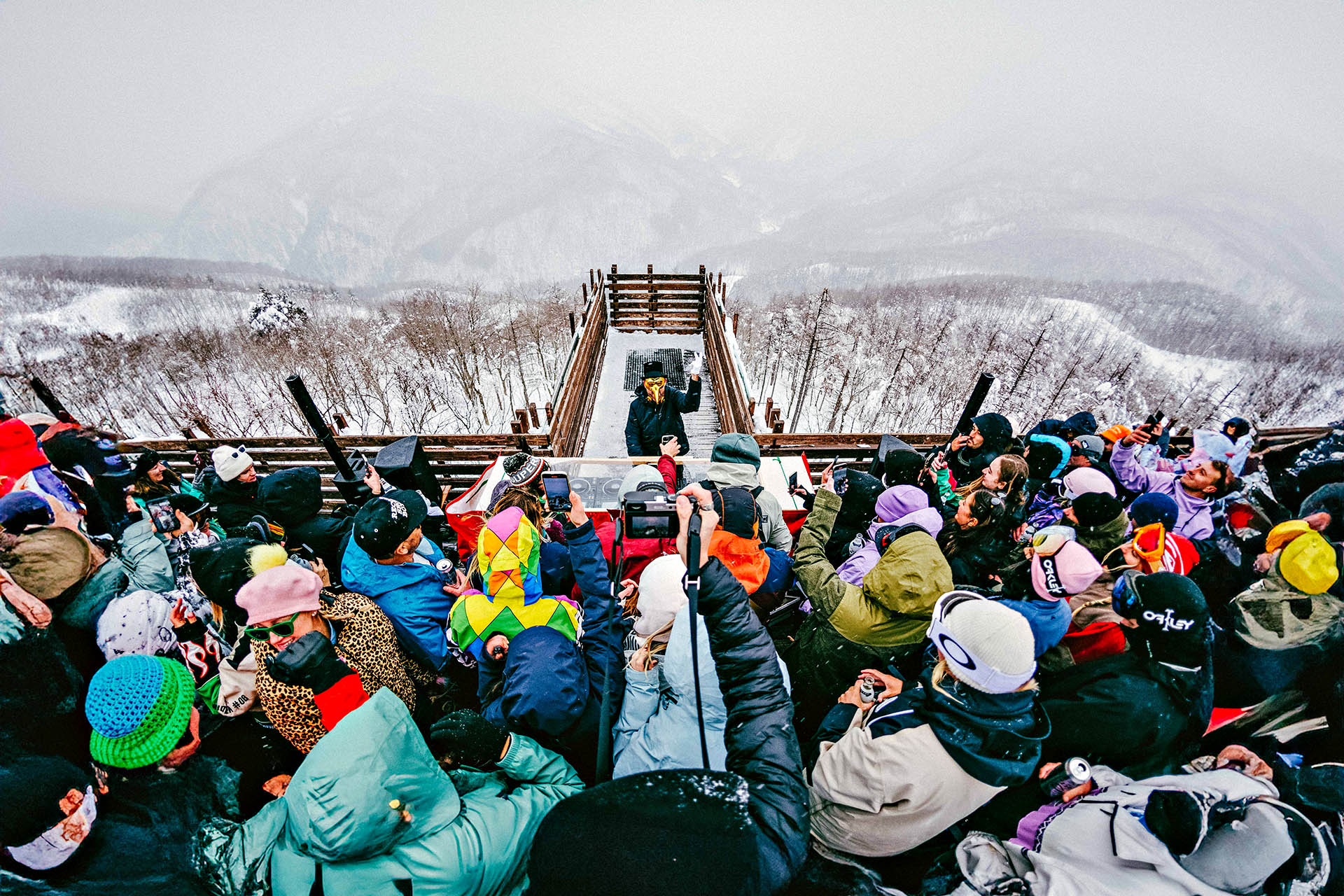 DJ performing to a packed crowd at a mountaintop Snow Machine event overlooking the snow-covered mountains of Hakuba, Japan.