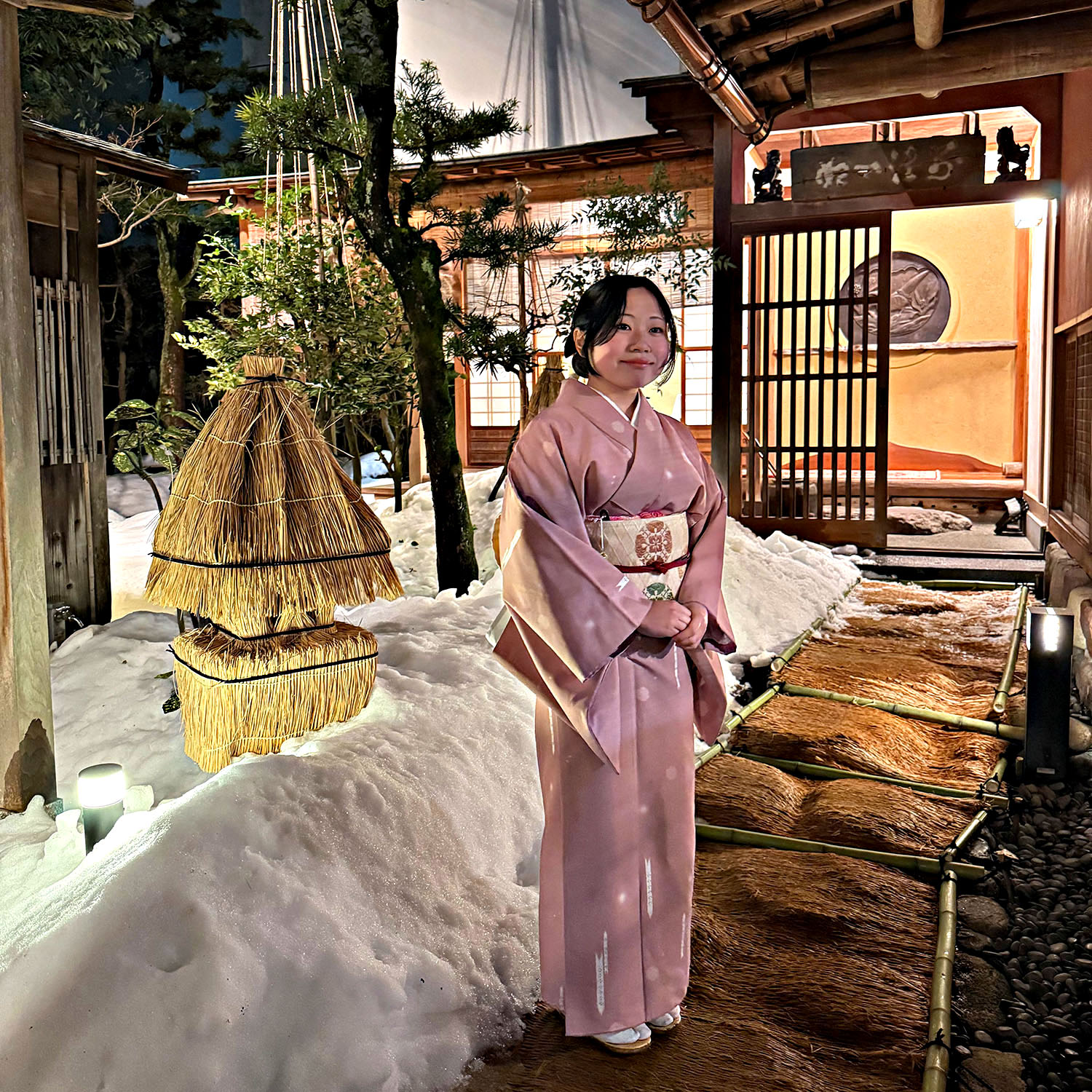 Woman wearing a traditional pink kimono in a snow-covered Japanese garden in Kanazawa.