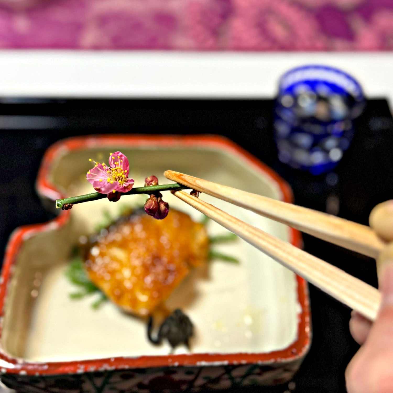 Delicate edible plum blossom held with chopsticks during a traditional Kaga cuisine meal in Kanazawa.