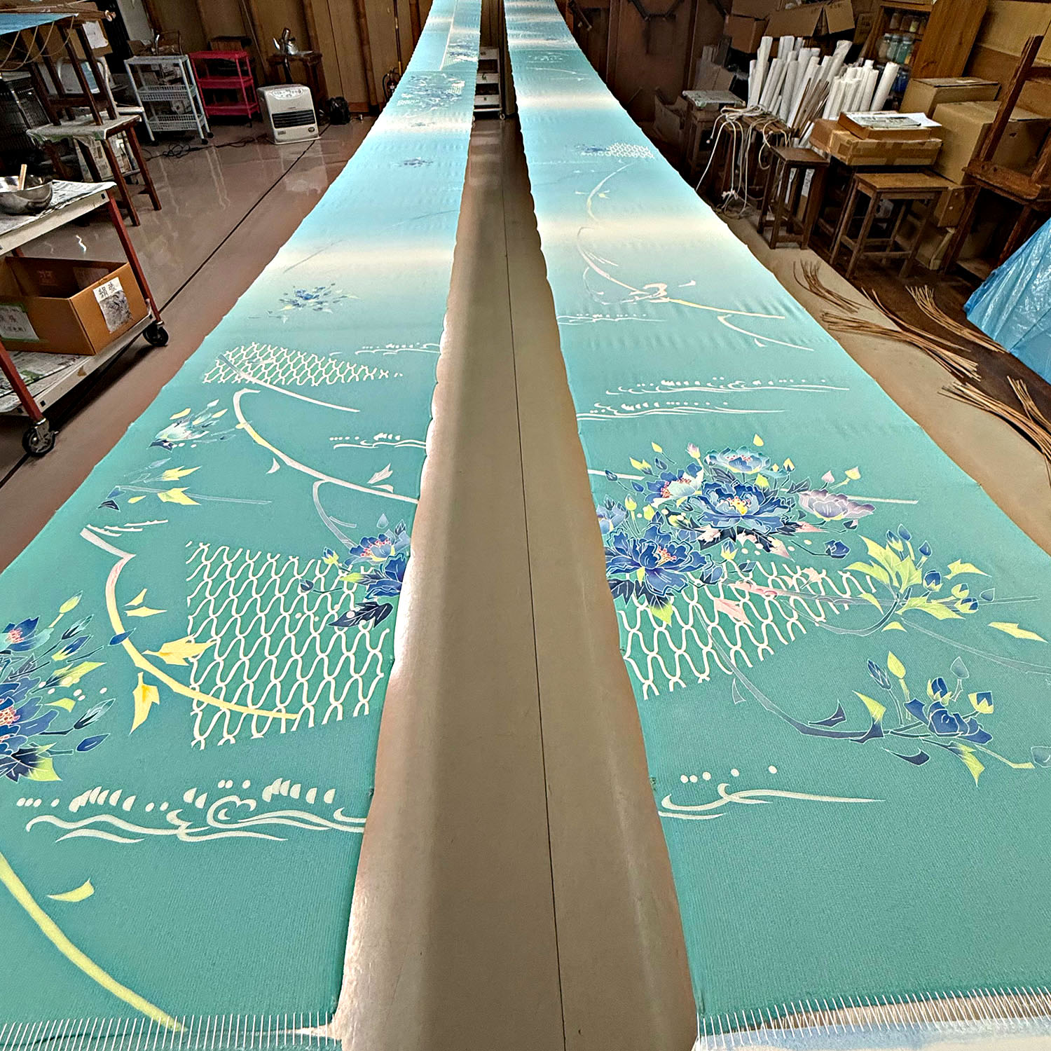 Long lengths of intricately patterned turquoise kimono fabric inside a Kanazawa textile workshop.