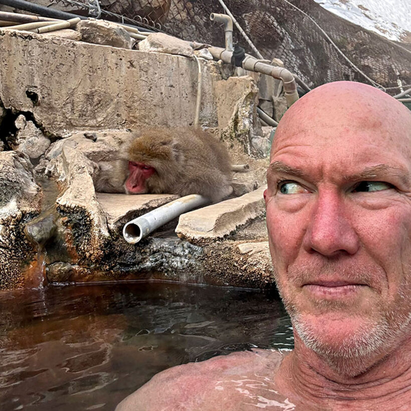 Traveller soaking in an outdoor onsen beside a Japanese snow monkey in Nagano, Japan.