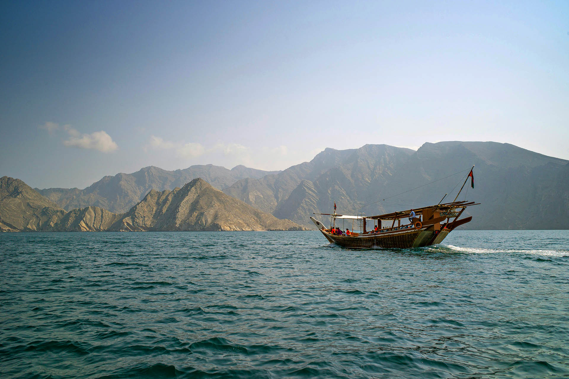 Traditional wooden dhow sailing across the Gulf of Oman with the dramatic Hajar Mountains in the background.