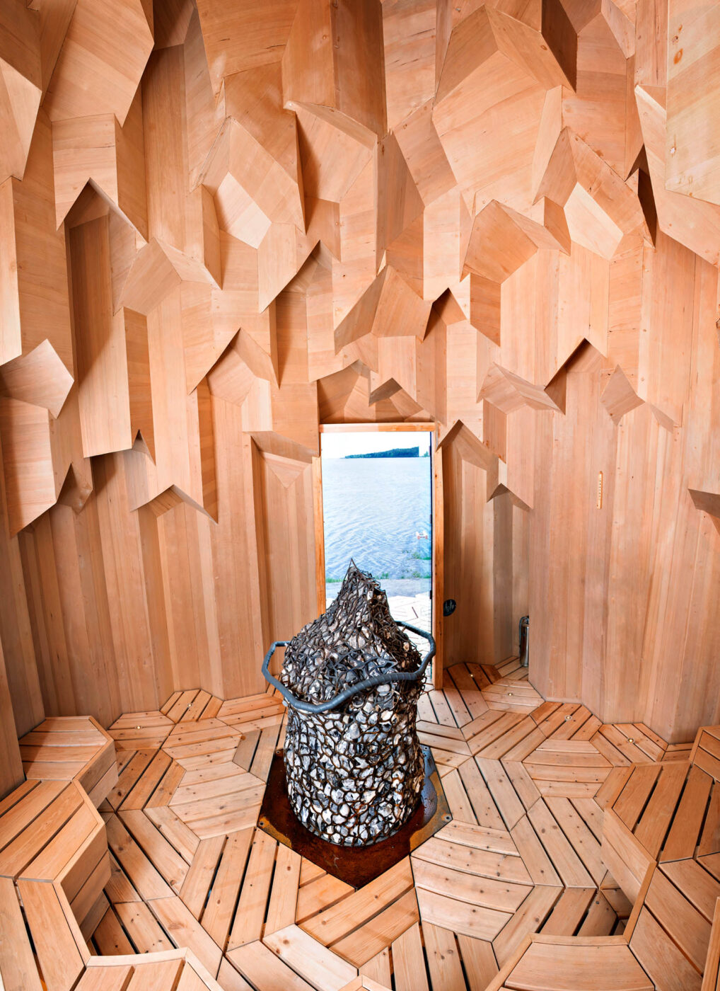 Timber interior and large stone-filled heater inside the Crystal Sauna overlooking the Skellefte River in Sweden.