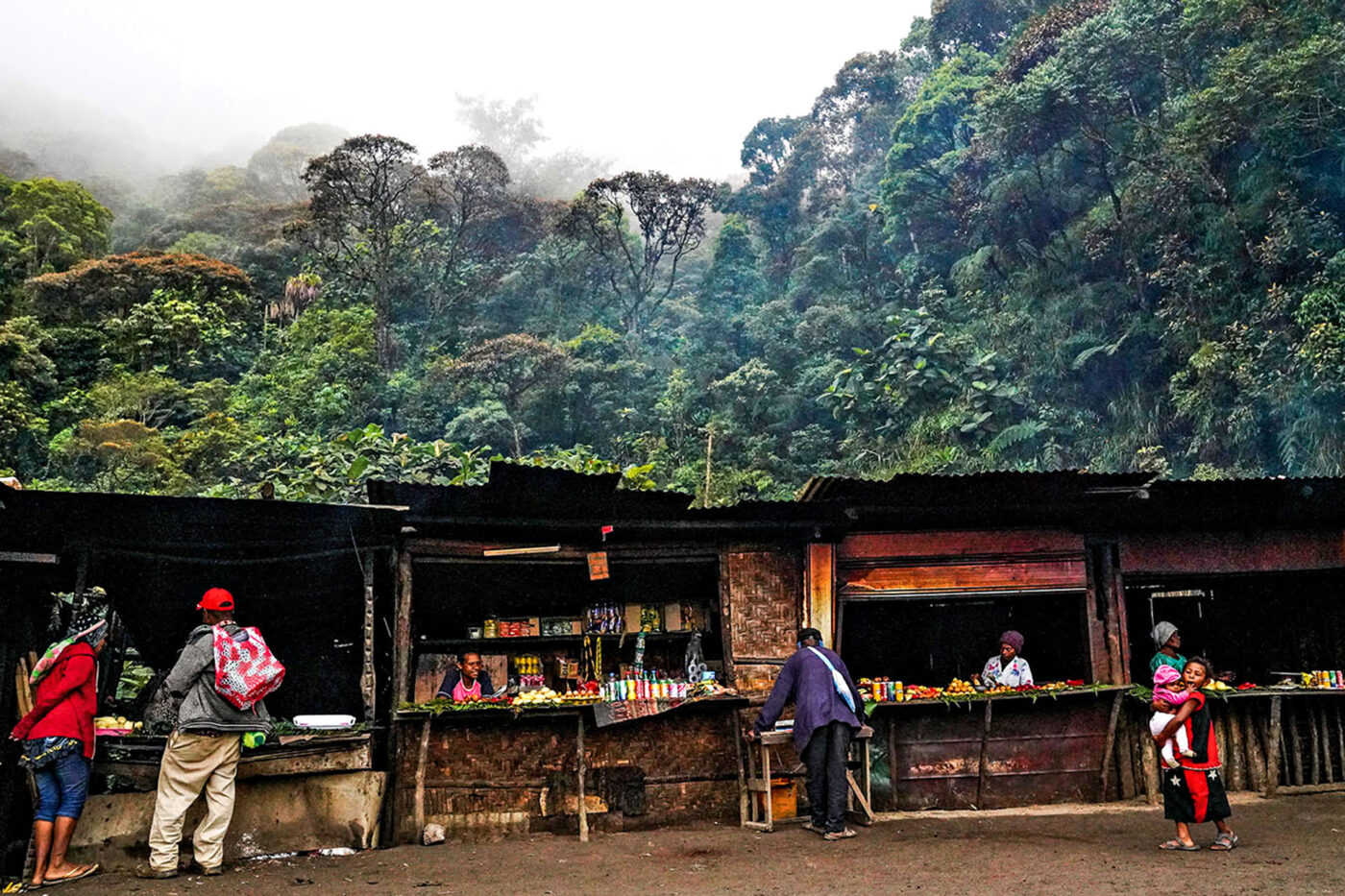 Roadside market stalls beneath misty rainforest in the Western Highlands near Mount Hagen, Papua New Guinea.