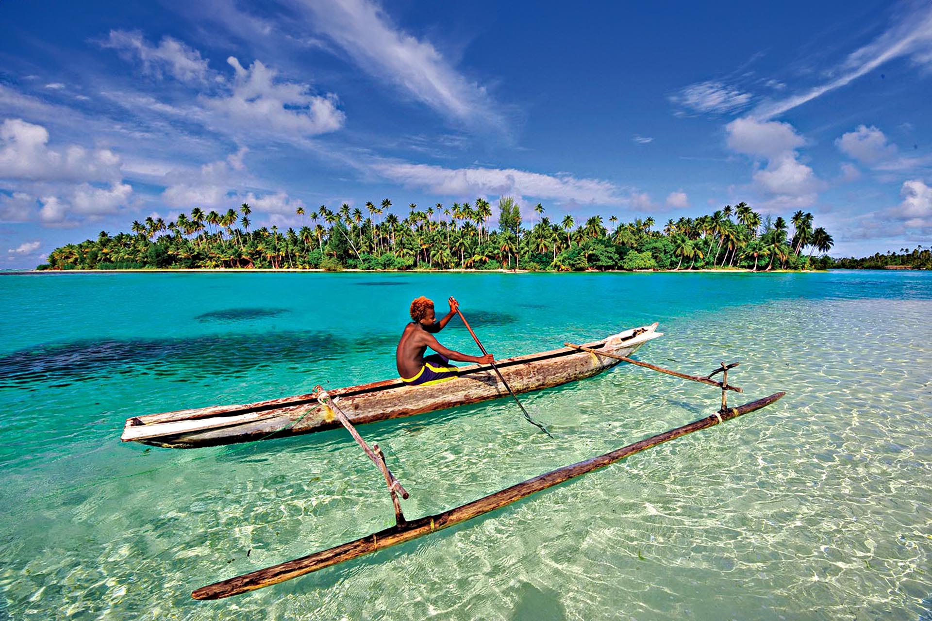 Local paddler navigating a traditional outrigger canoe through clear turquoise water in Papua New Guinea.