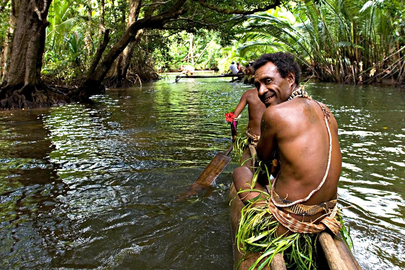 Local man paddling a dugout canoe along a rainforest-lined river in Papua New Guinea.