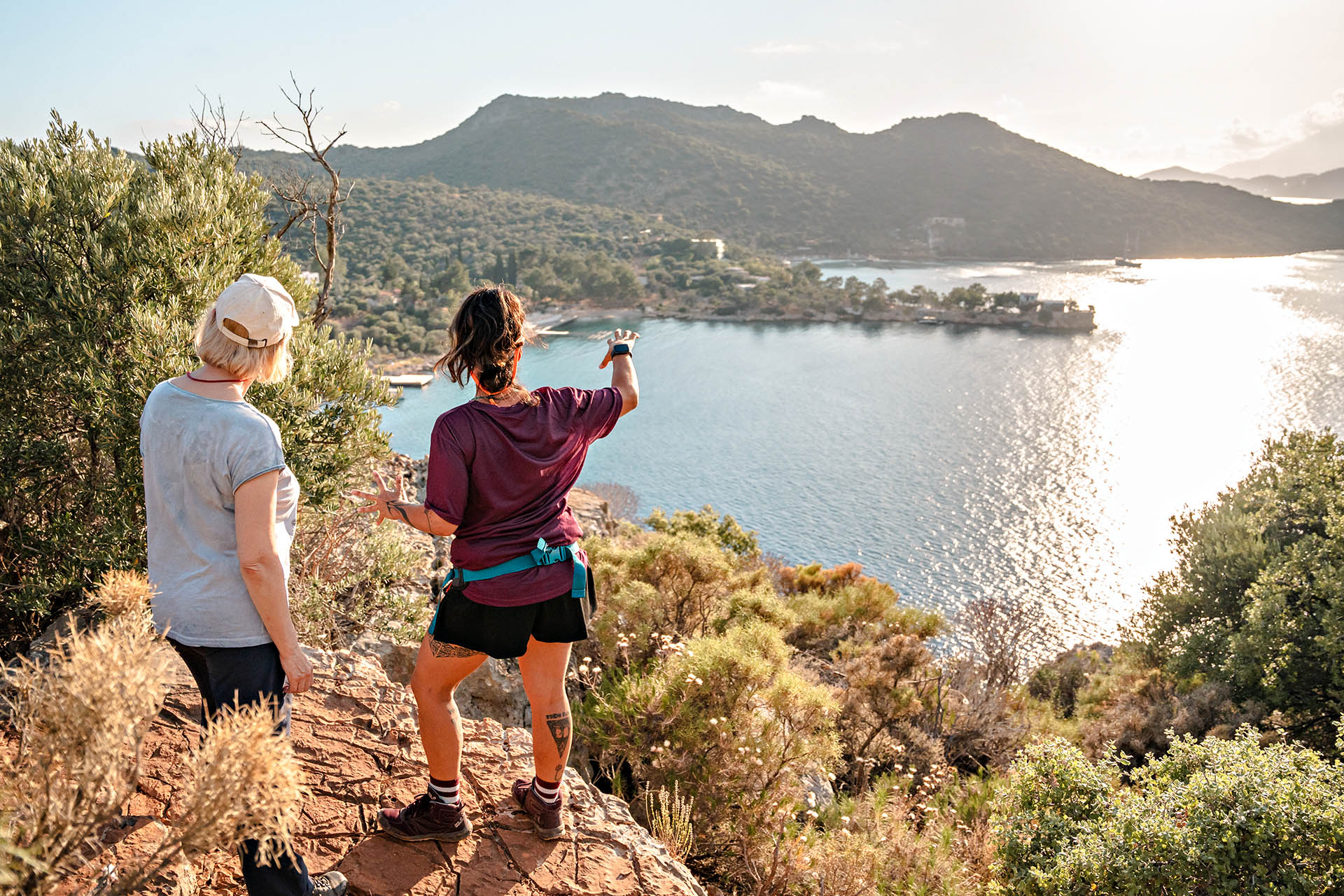 Two women hiking above a sunlit coastal bay on an Explore Worldwide small-group adventure.