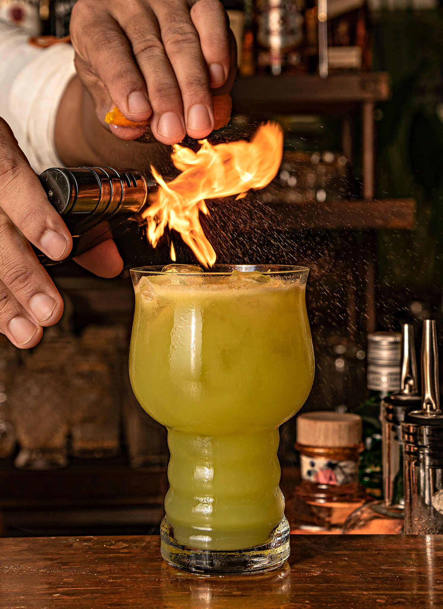 Bartender flaming a garnish over a Herbal Kulen Gin cocktail at Scribe Bar.