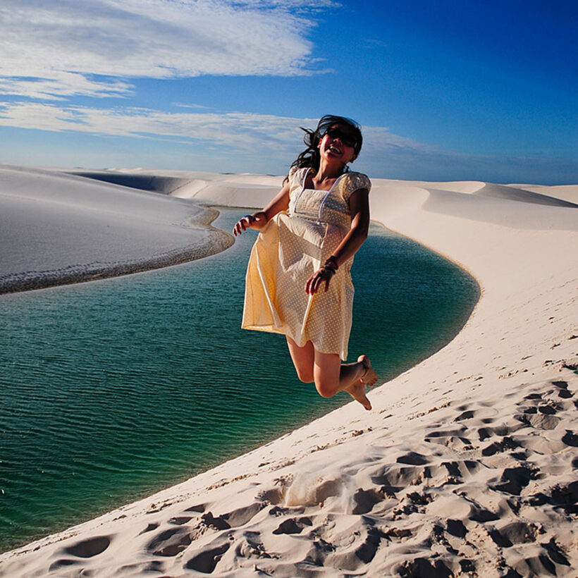 Traveller jumping from a white sand dune above a turquoise lagoon in Lençóis Maranhenses.