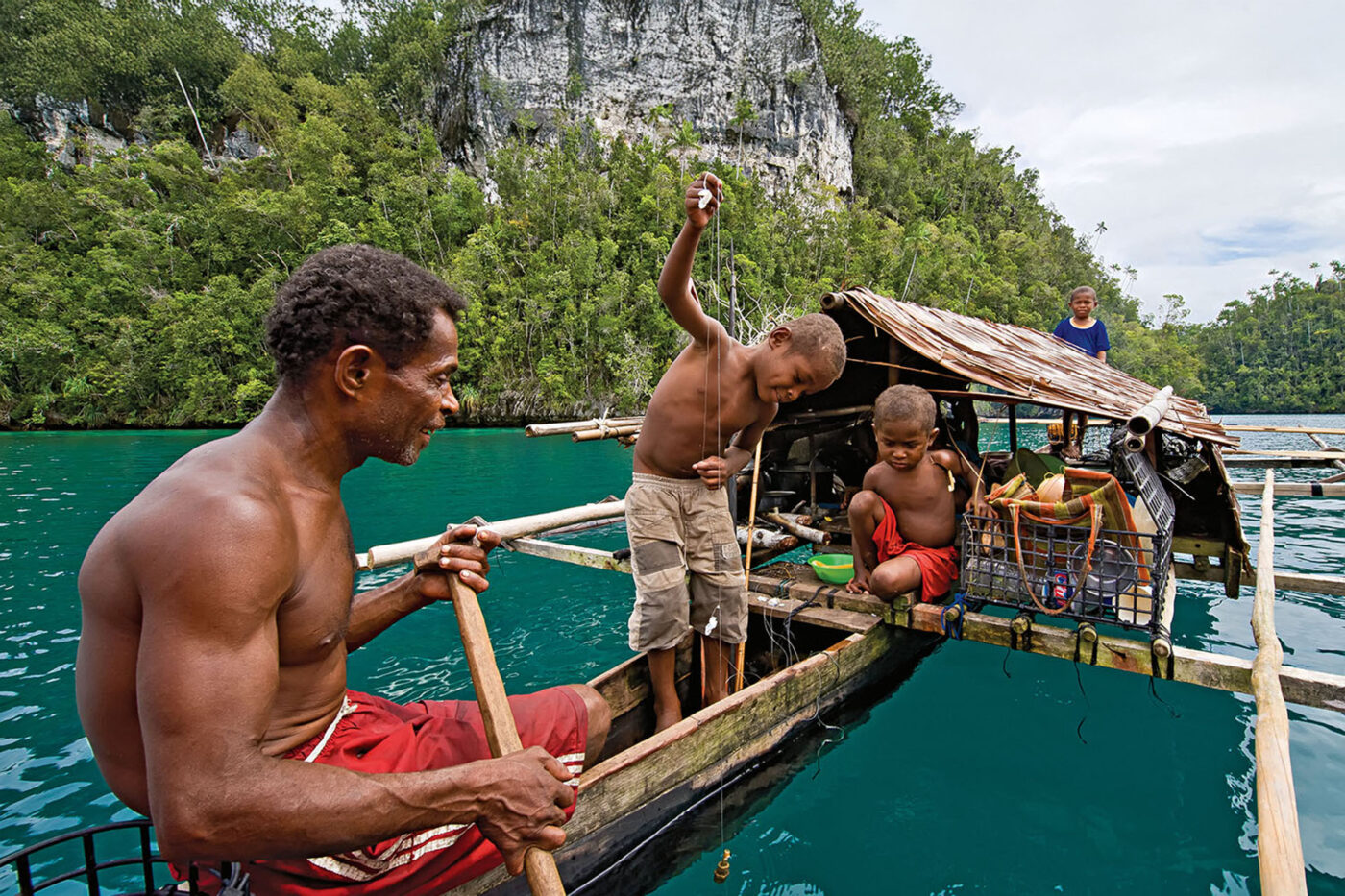 A family fishes from a traditional wooden vessel.