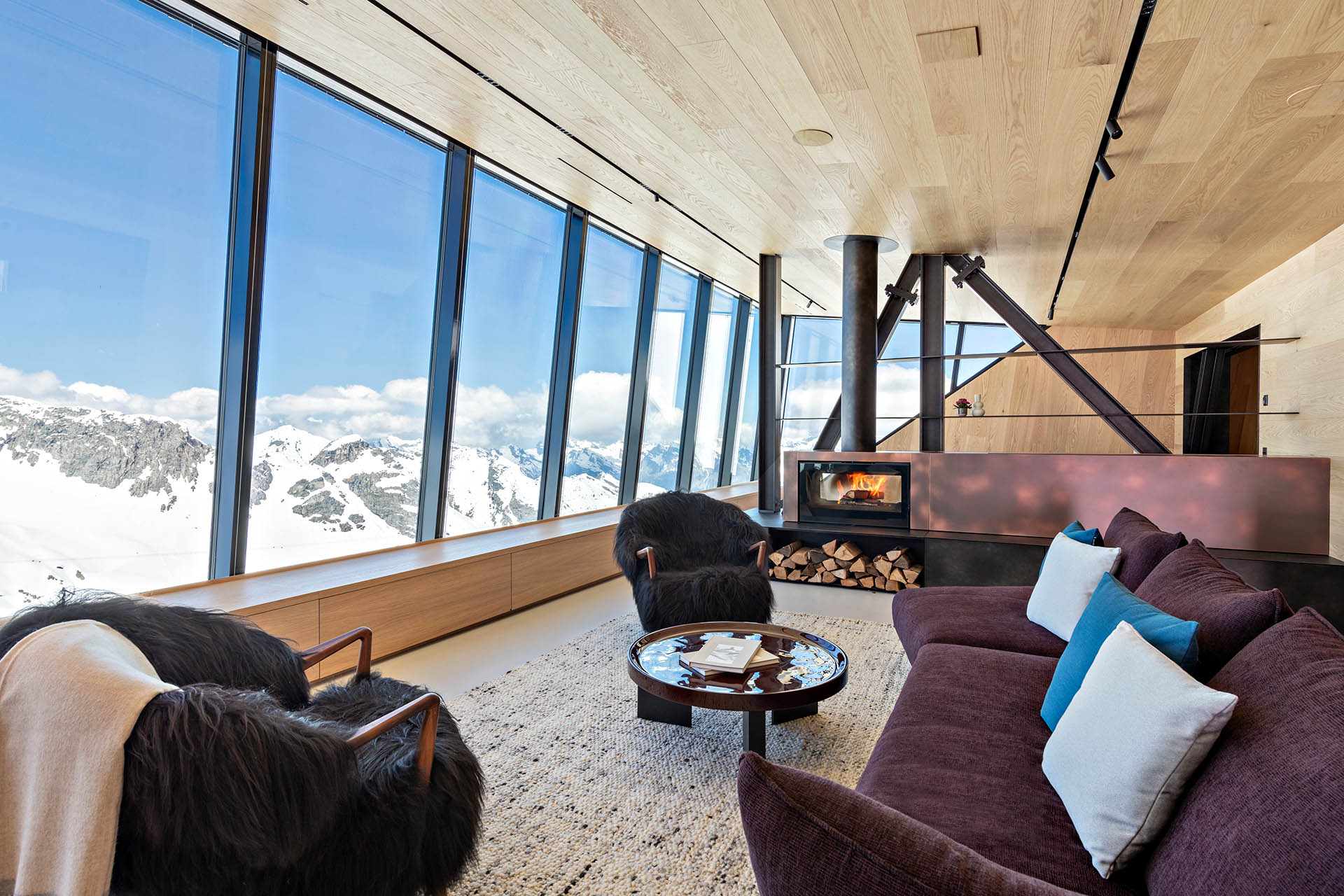 Cabane Tortin living room with a wood-burning fireplace and panoramic mountain views in Verbier, Switzerland.