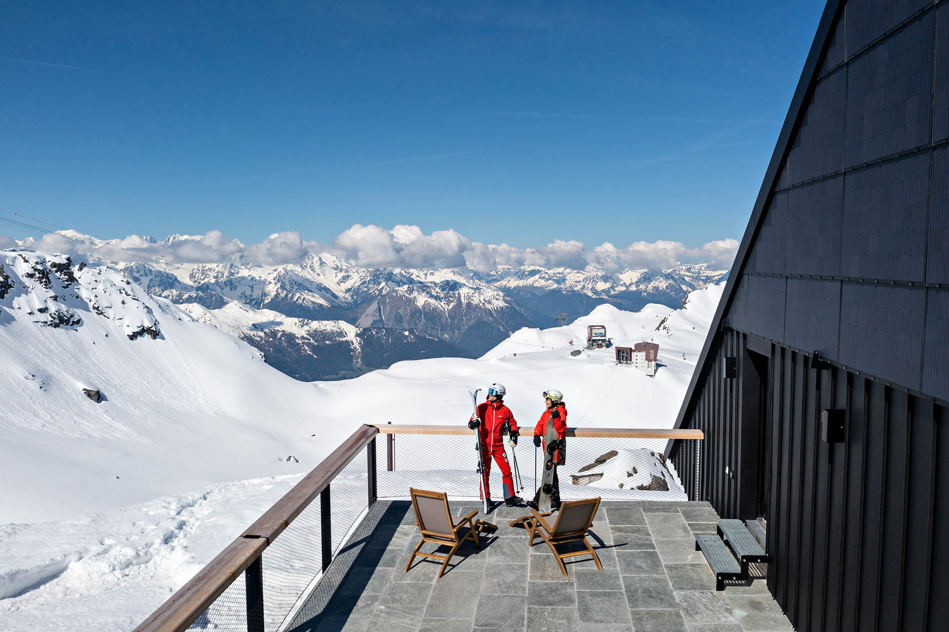 Skiers outside Cabane Tortin overlooking the snow-covered mountains of Verbier in the Swiss Alps.