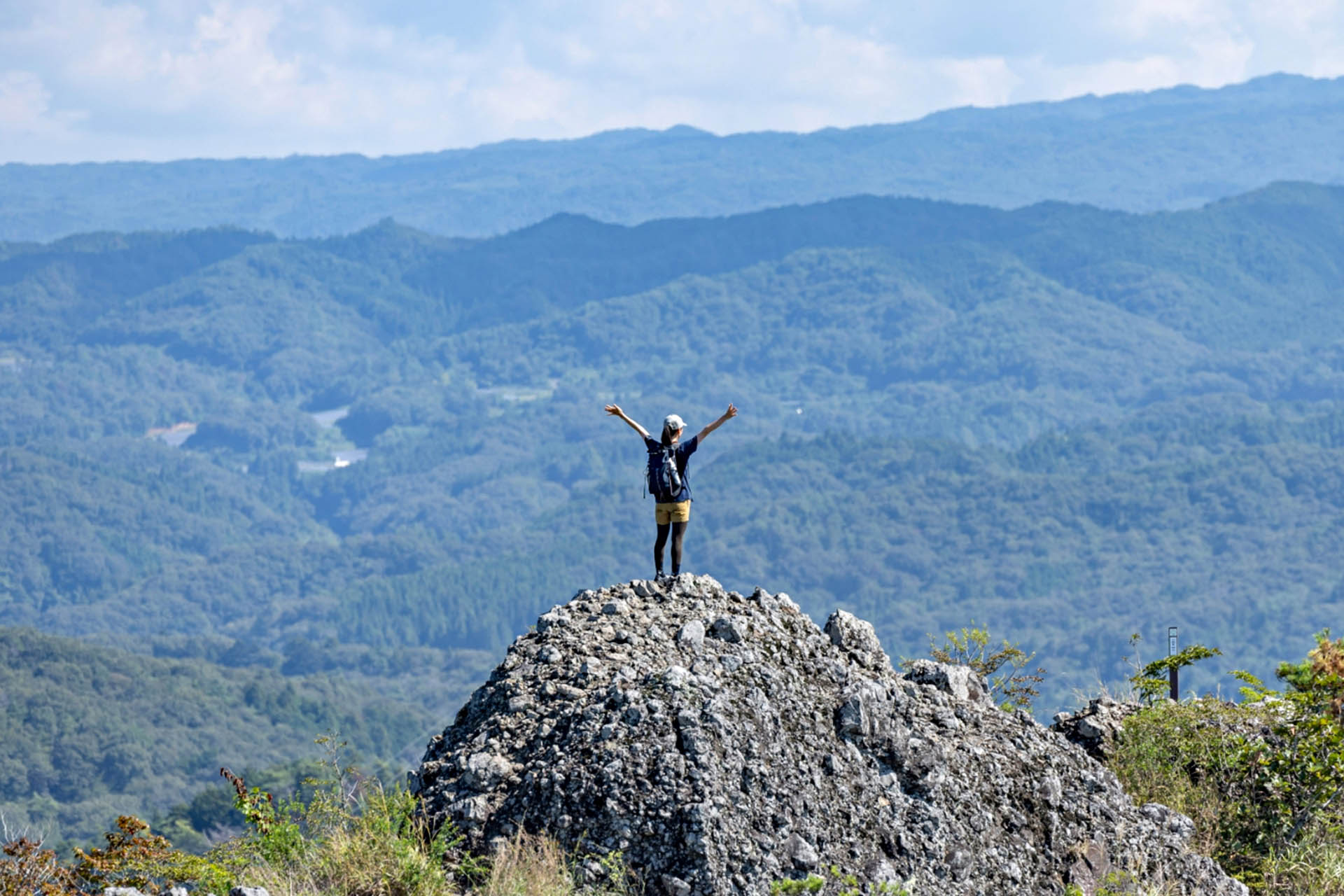 Hiker standing on a rocky mountain summit along the Hitachi-no-Kuni Long Trail in Ibaraki Prefecture, Japan.