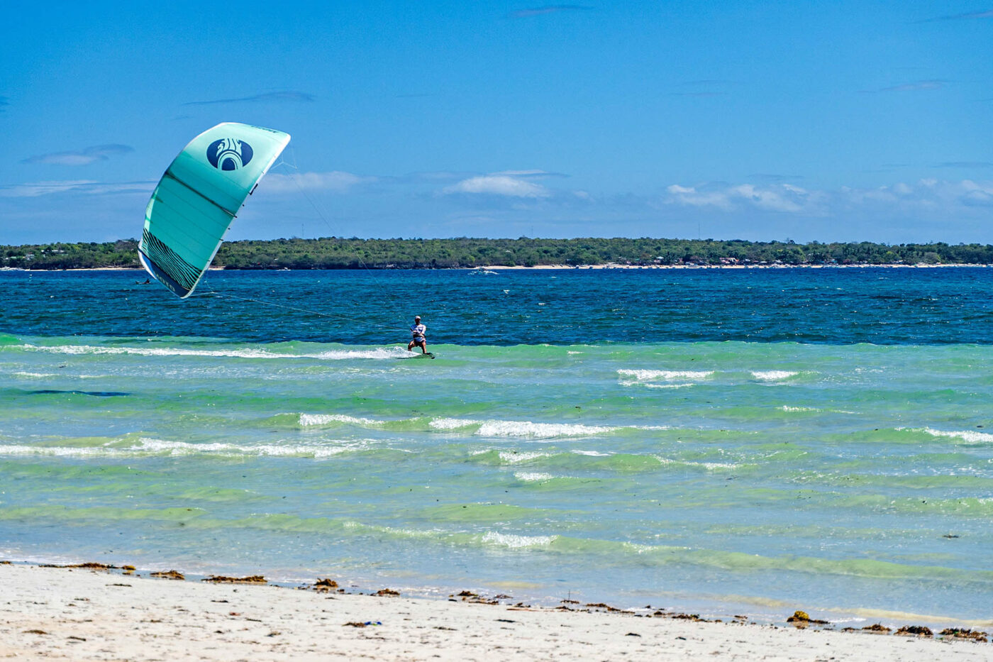 Kitesurfer riding across clear blue water off a white sand beach in the Philippines.
