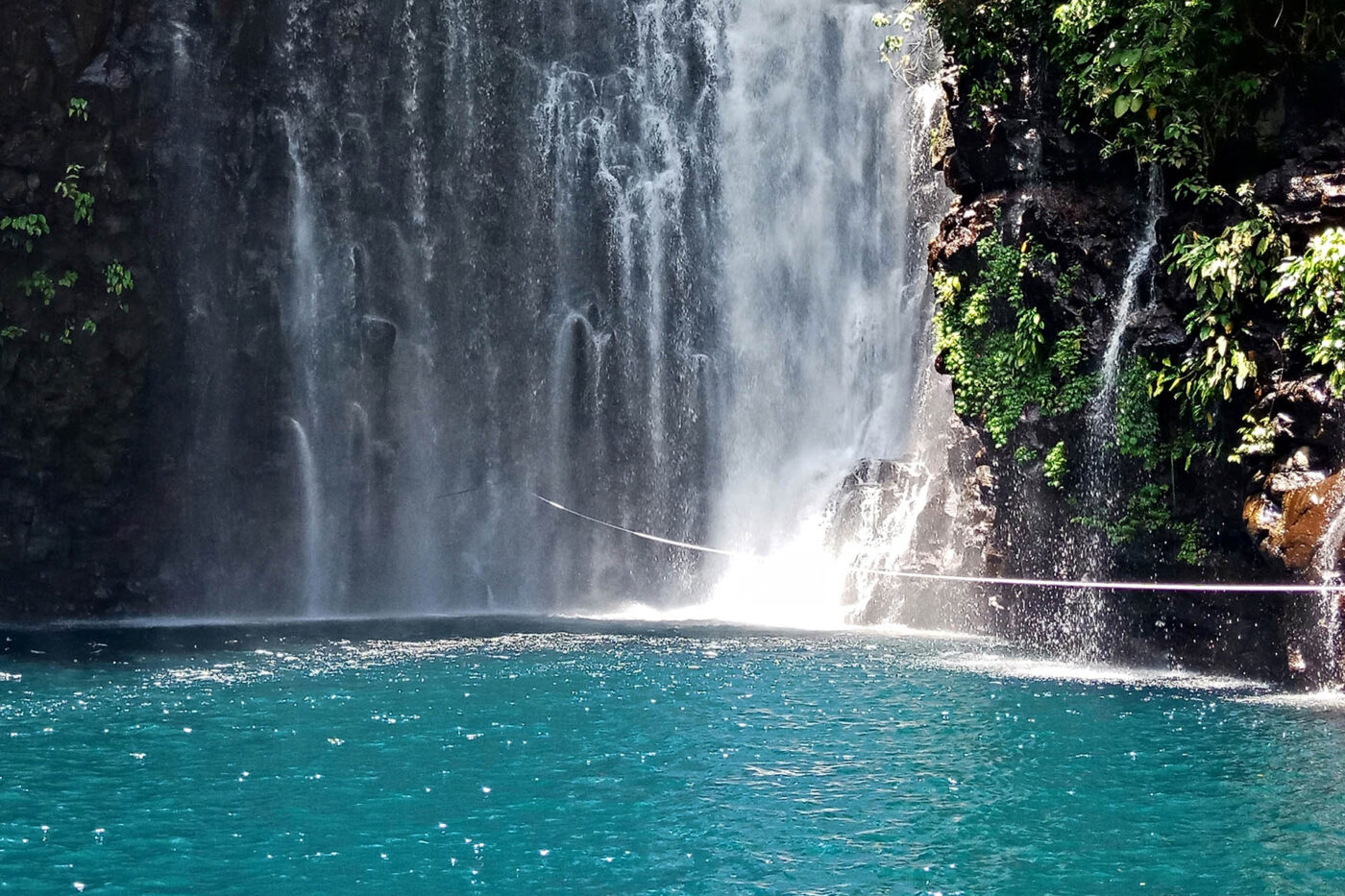 Waterfall plunging into a turquoise swimming hole surrounded by tropical rainforest in Biliran, Philippines.