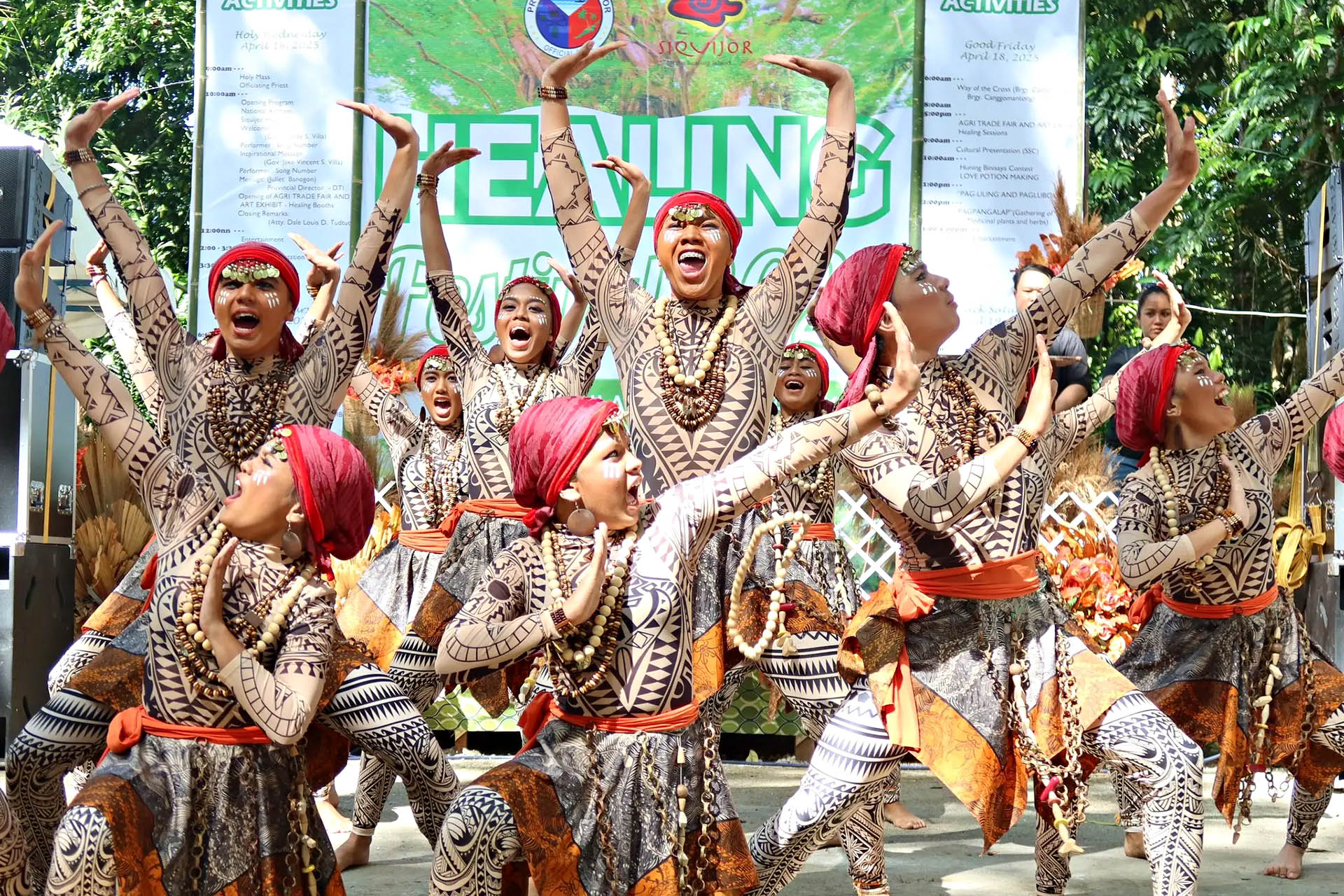 Traditional dancers performing in patterned costumes and red headscarves at a festival in the Philippines.
