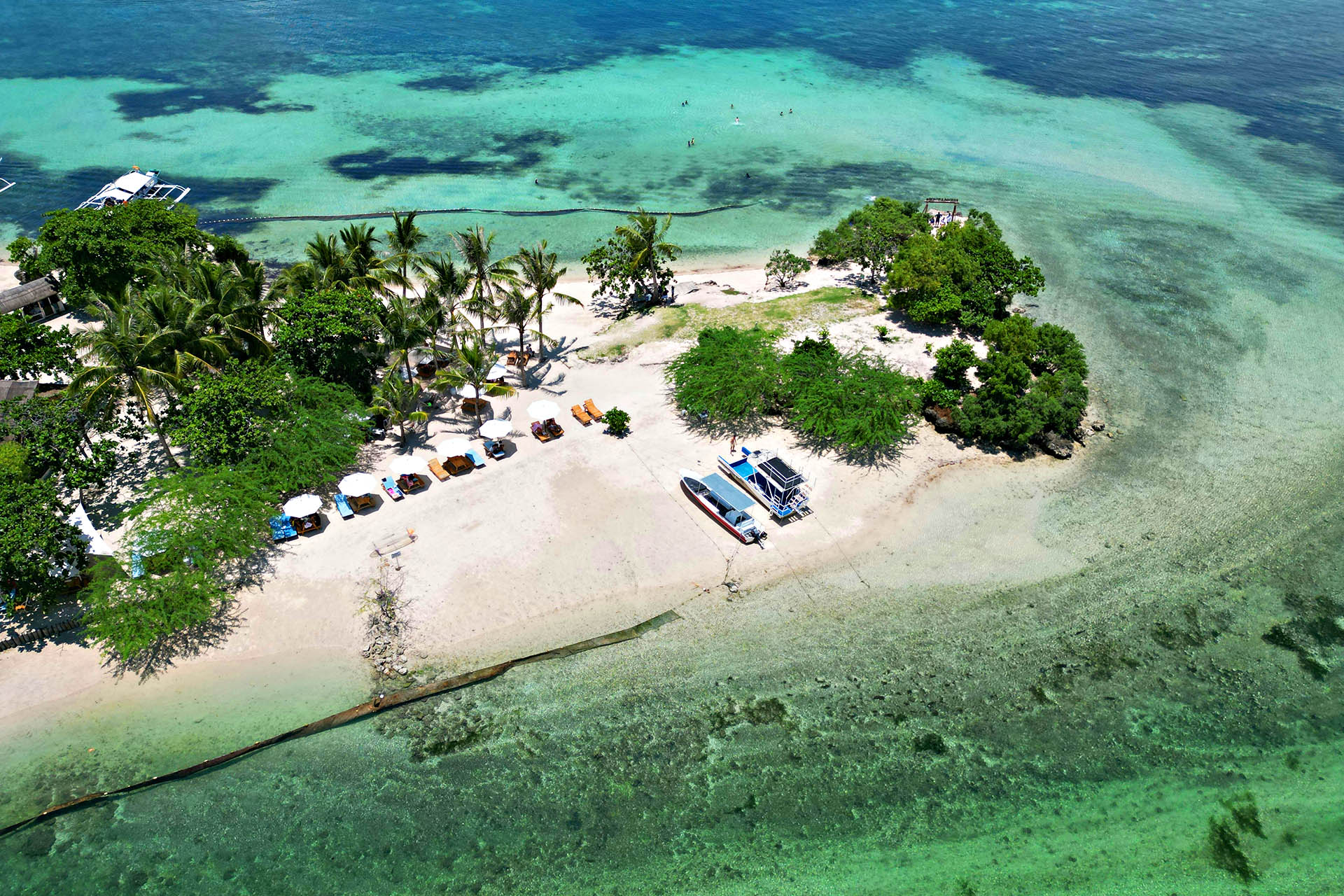 Aerial view of a white sand beach, boats and shallow turquoise water in the Philippines.