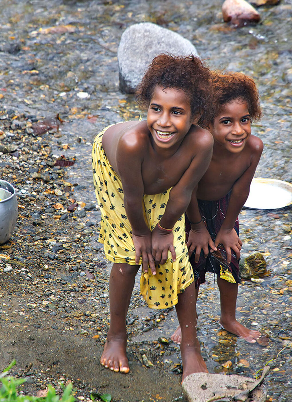 Two local kids smiling and posing for the camera with their hands on their knees.