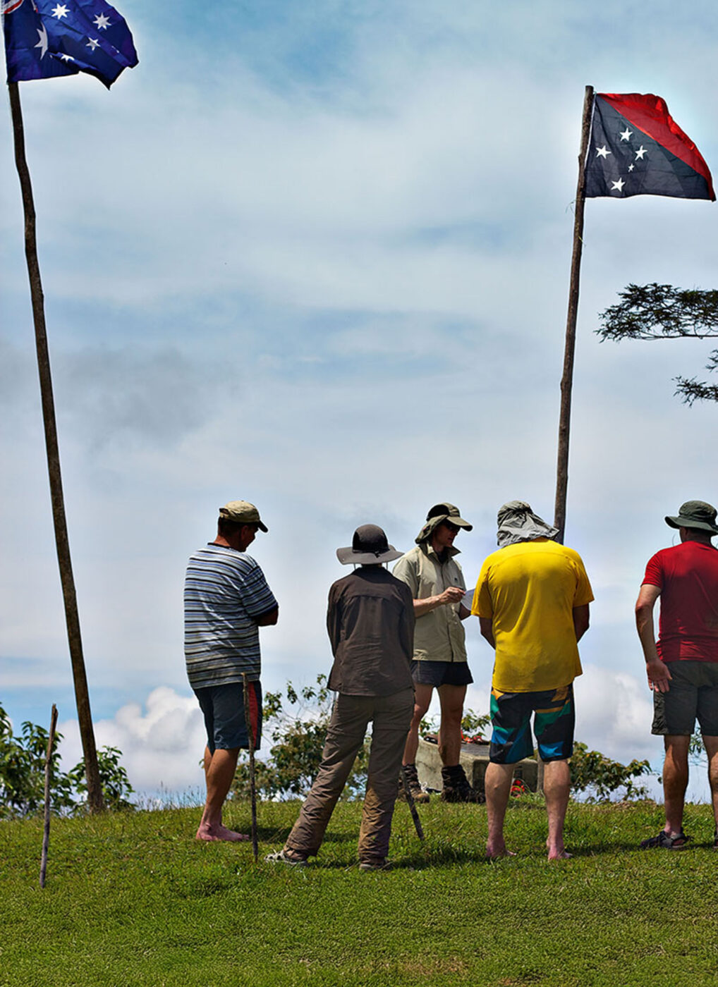 5 people standing on top of 'Brigade Hill' reflecting on the war. Australian and Papua New Guinea flags fly above them.