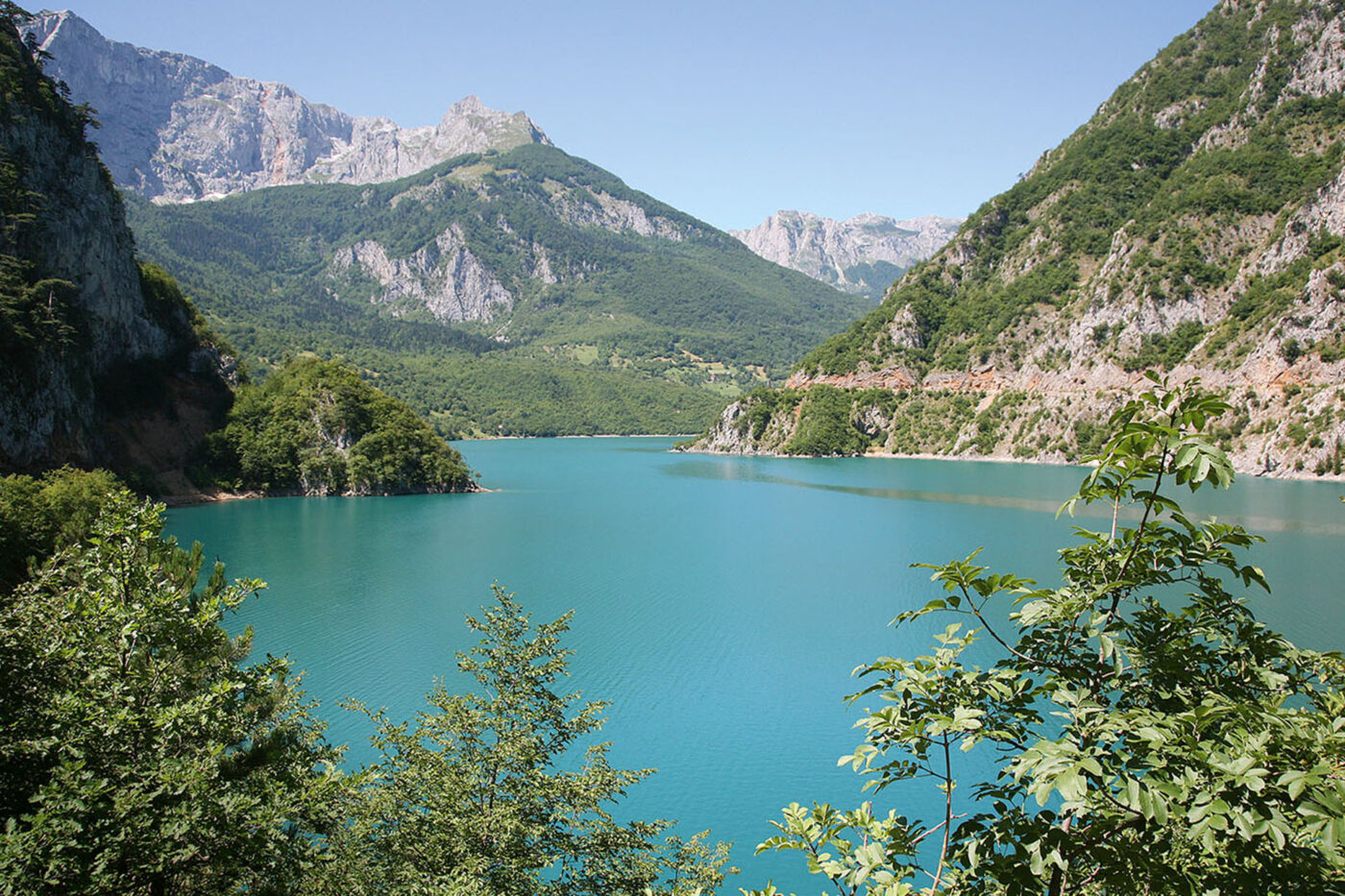 A landscape shot of a big blue lake surrounded by mountains and trees.