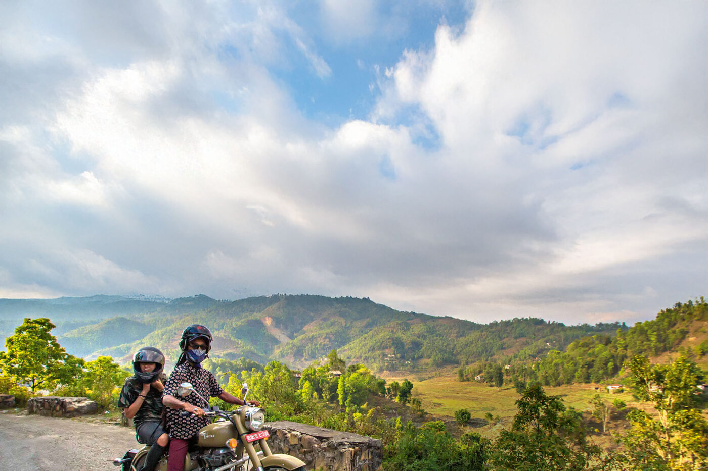 A mother and child riding a motorcycle, with a giant landscape of hills and mountains behind them.