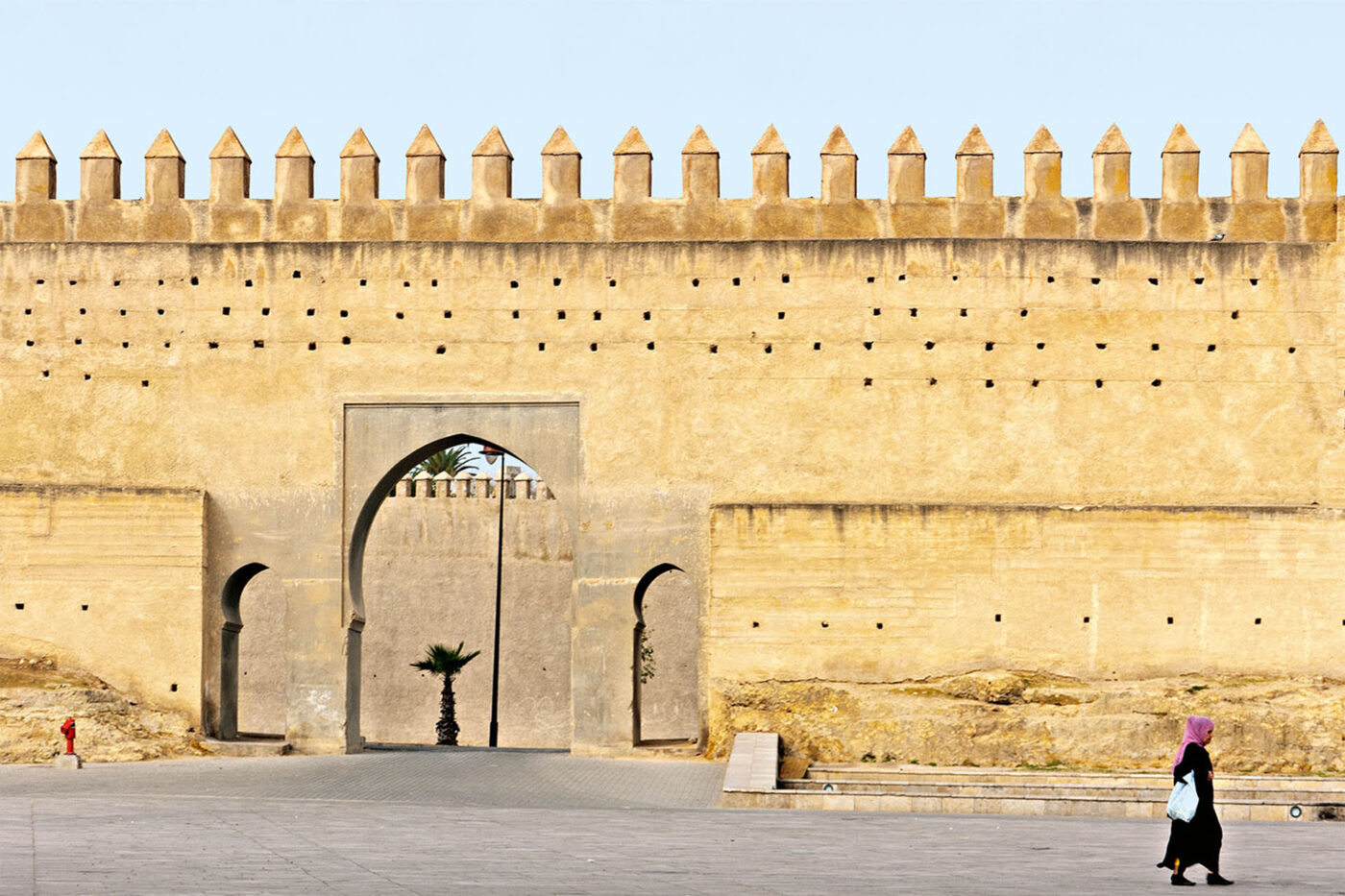 A woman walks ndown the street next to the ancient walls of Fez medina.
