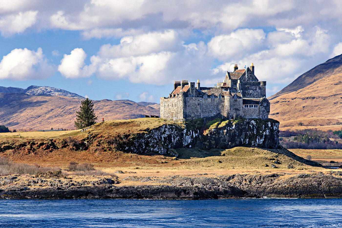 A grand grey castle up on a hill, looking over the ocean.