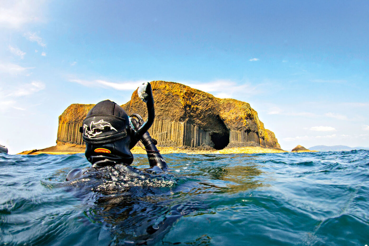 A snorkeler coming up for air, and looking at a big yellow rock formation in the middle of the ocean.