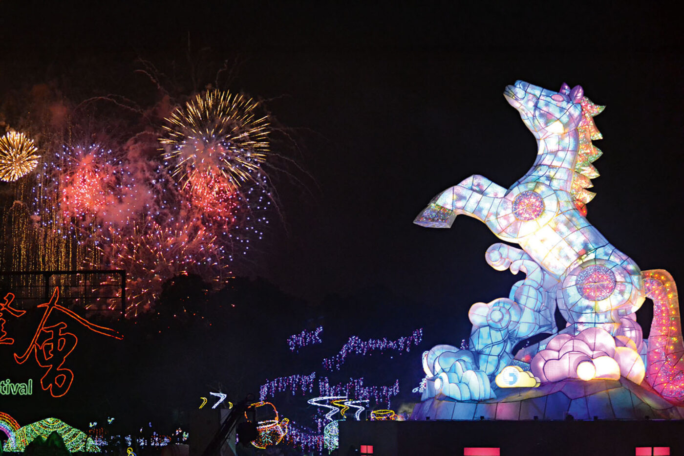 A lightup horse with it's front legs raise up. Next to it, a red and yellow fireworks show.