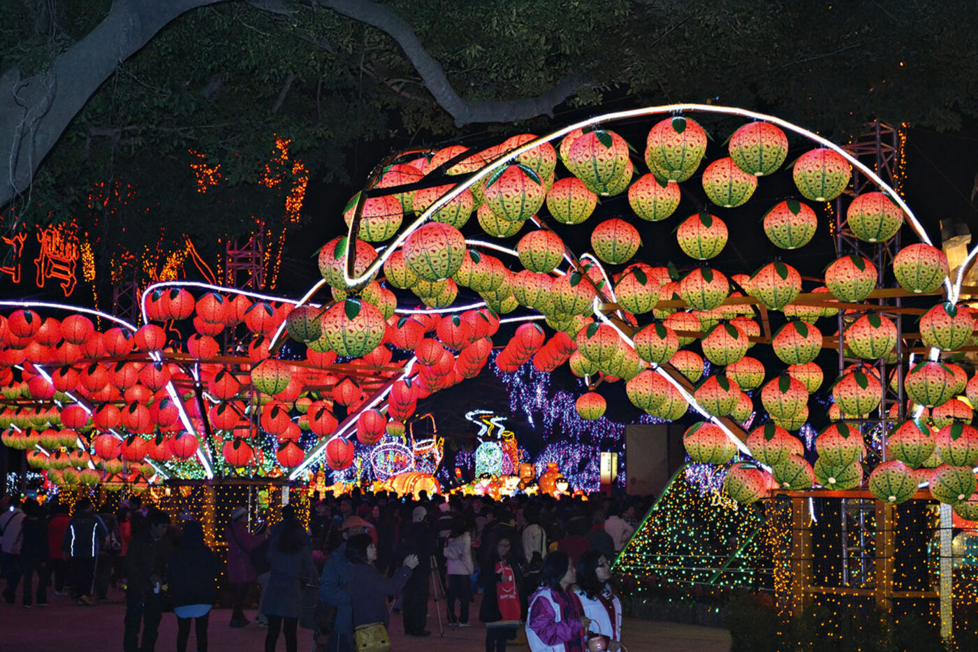 Lanterns in the shape of round fruits, hung up above crowds of people.