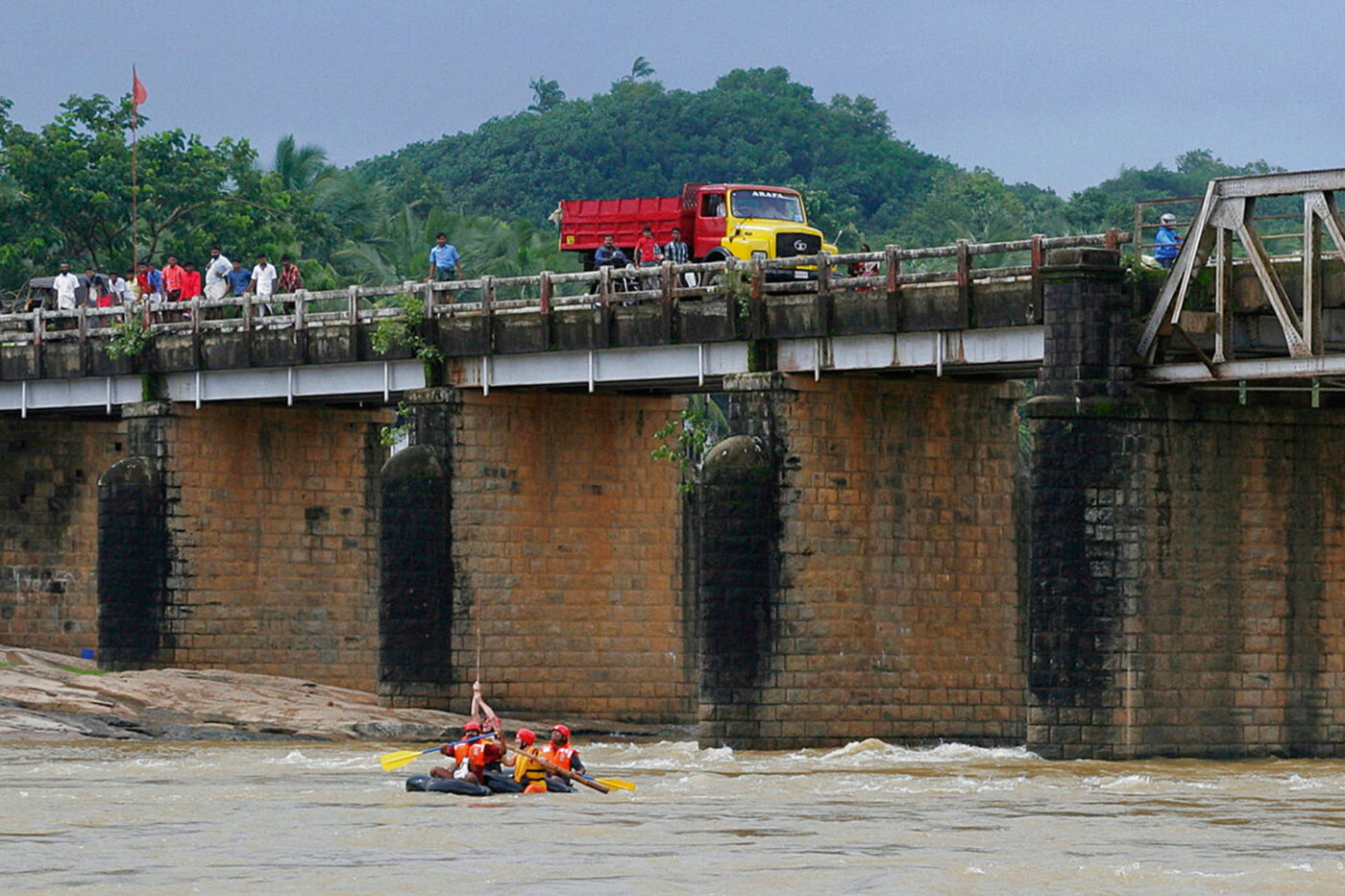 The group on the floating device going under a large bridge with cars and people on top of it.