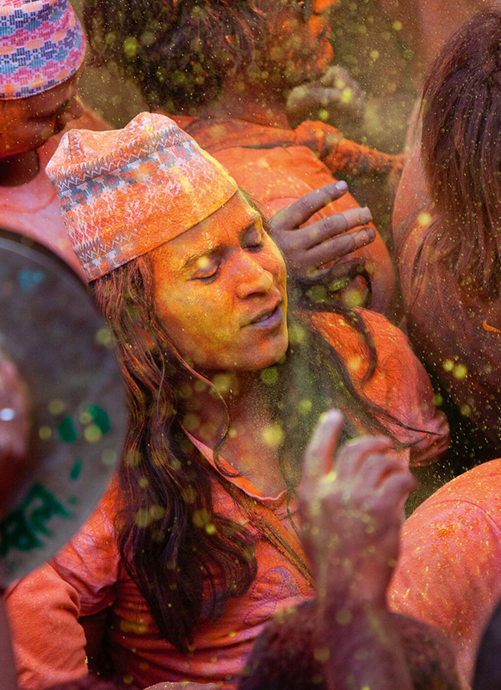 A person who's face is covered in orange powder, feeling ecstasy in the middle of the crowd.