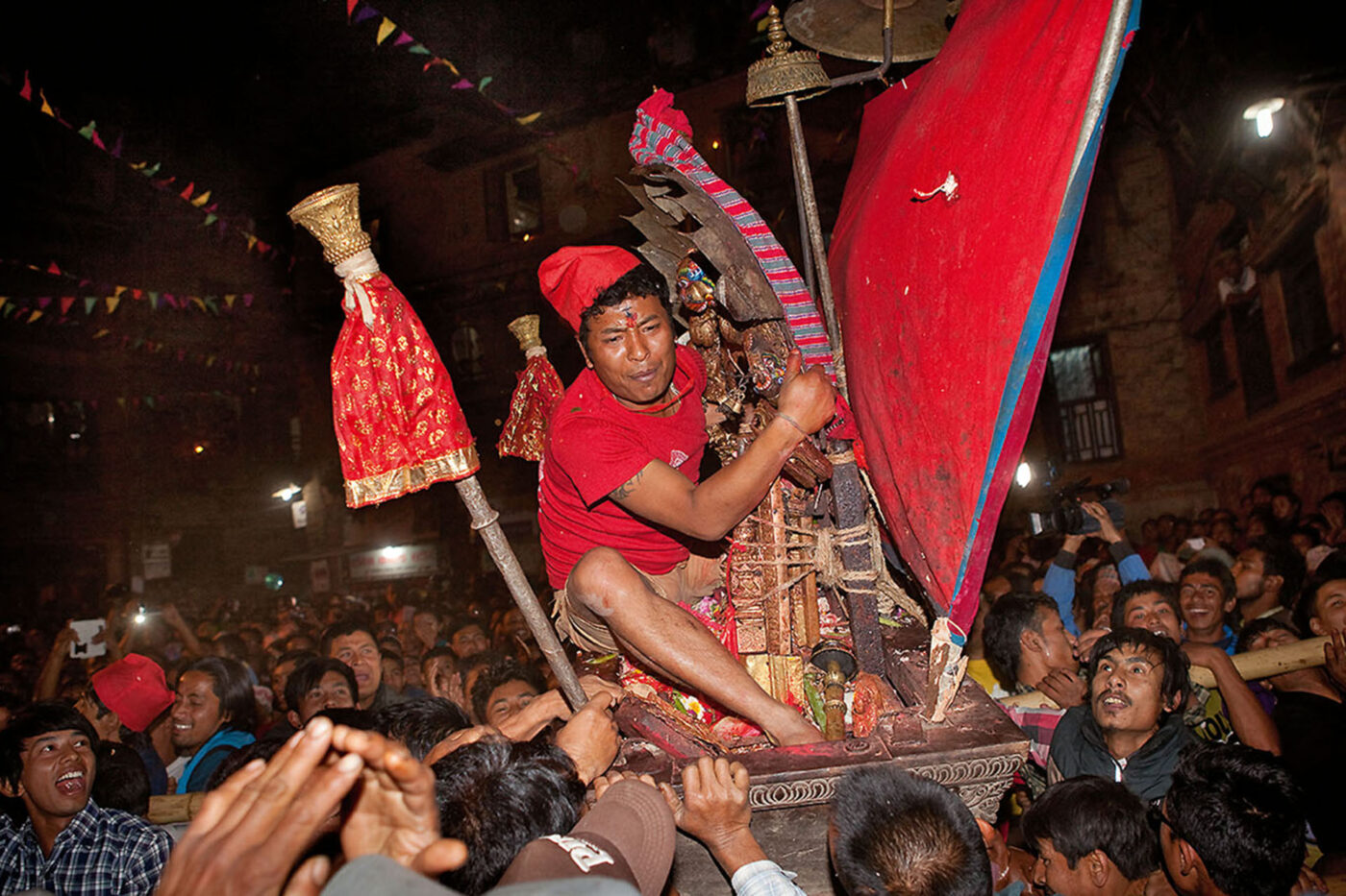 A man clutching onto the khat as it's being carried by a big group of people.