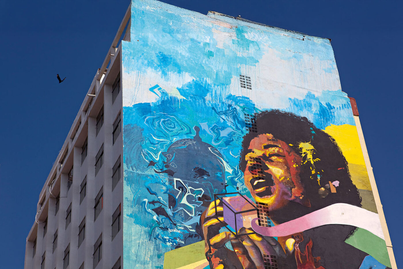A colourful mural on the side of a building depicting an Afro-Colombian person holding a cube.
