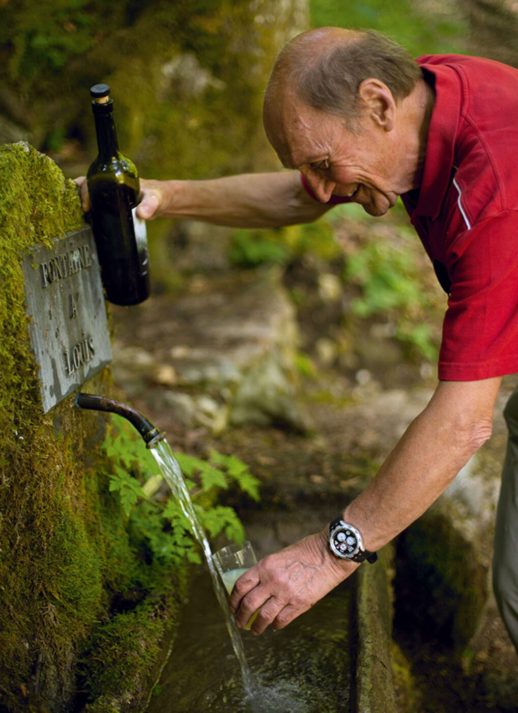 A man filling a glass with spring water from an outside tap.