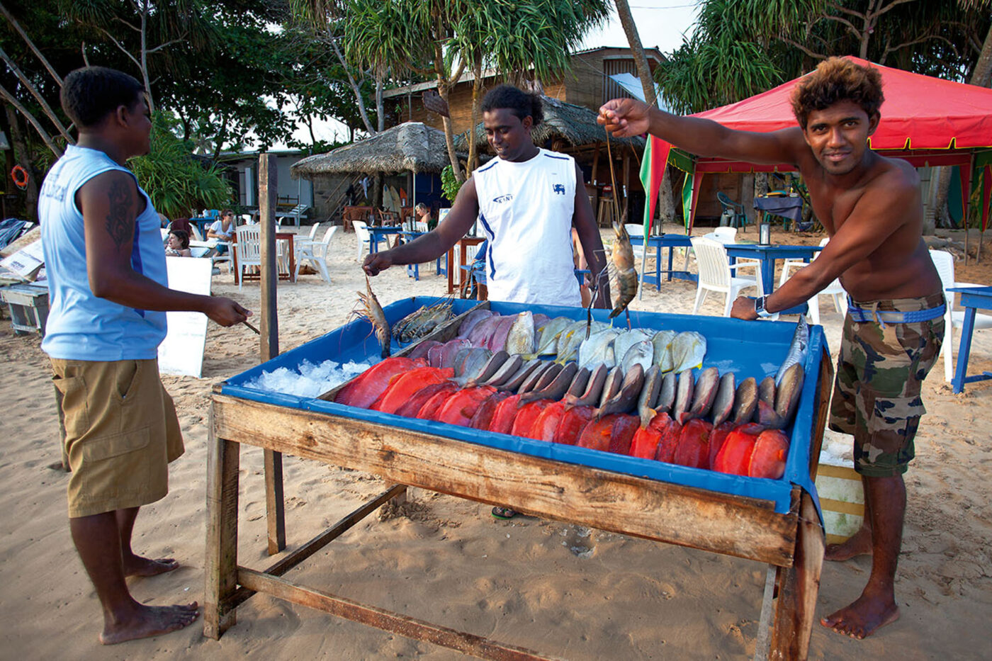 Three local men posing next to a table full of fish.