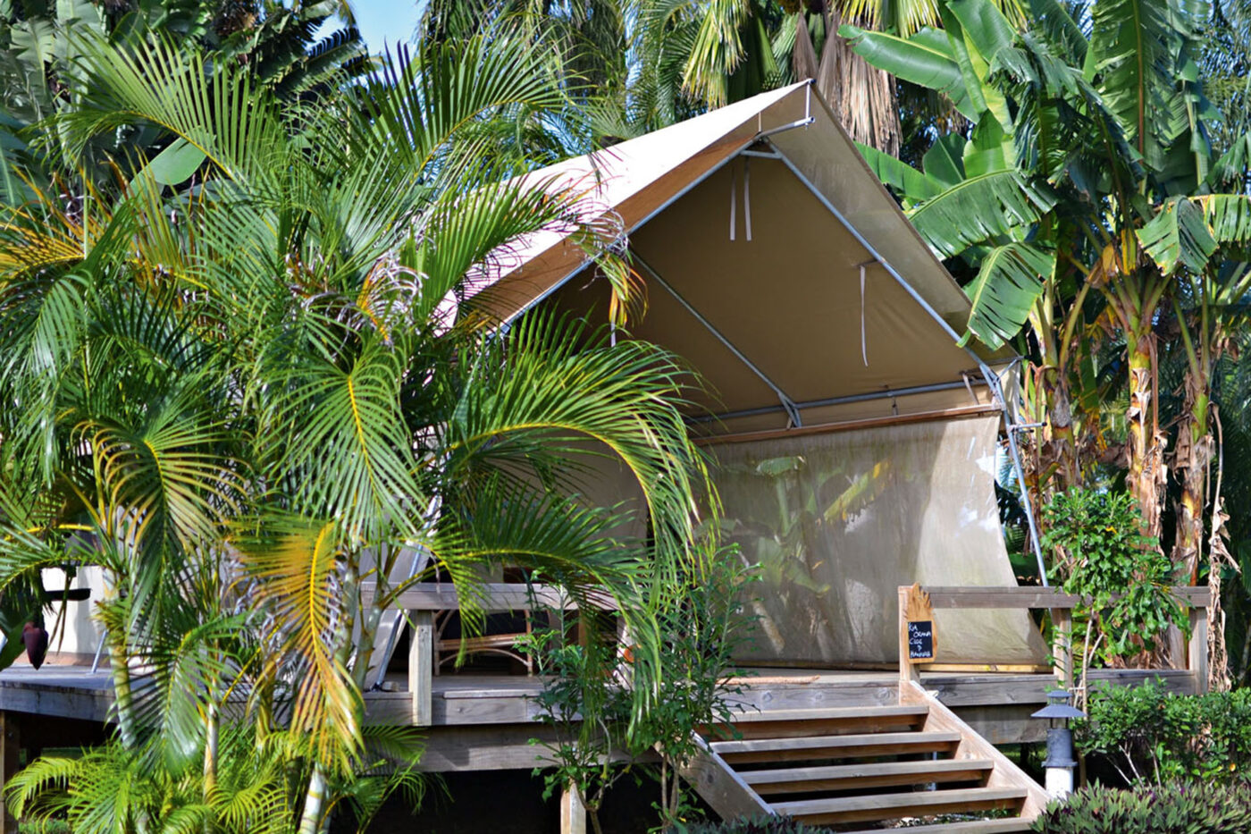 An open cabin surrounded by greenery. Stairs lead up to it