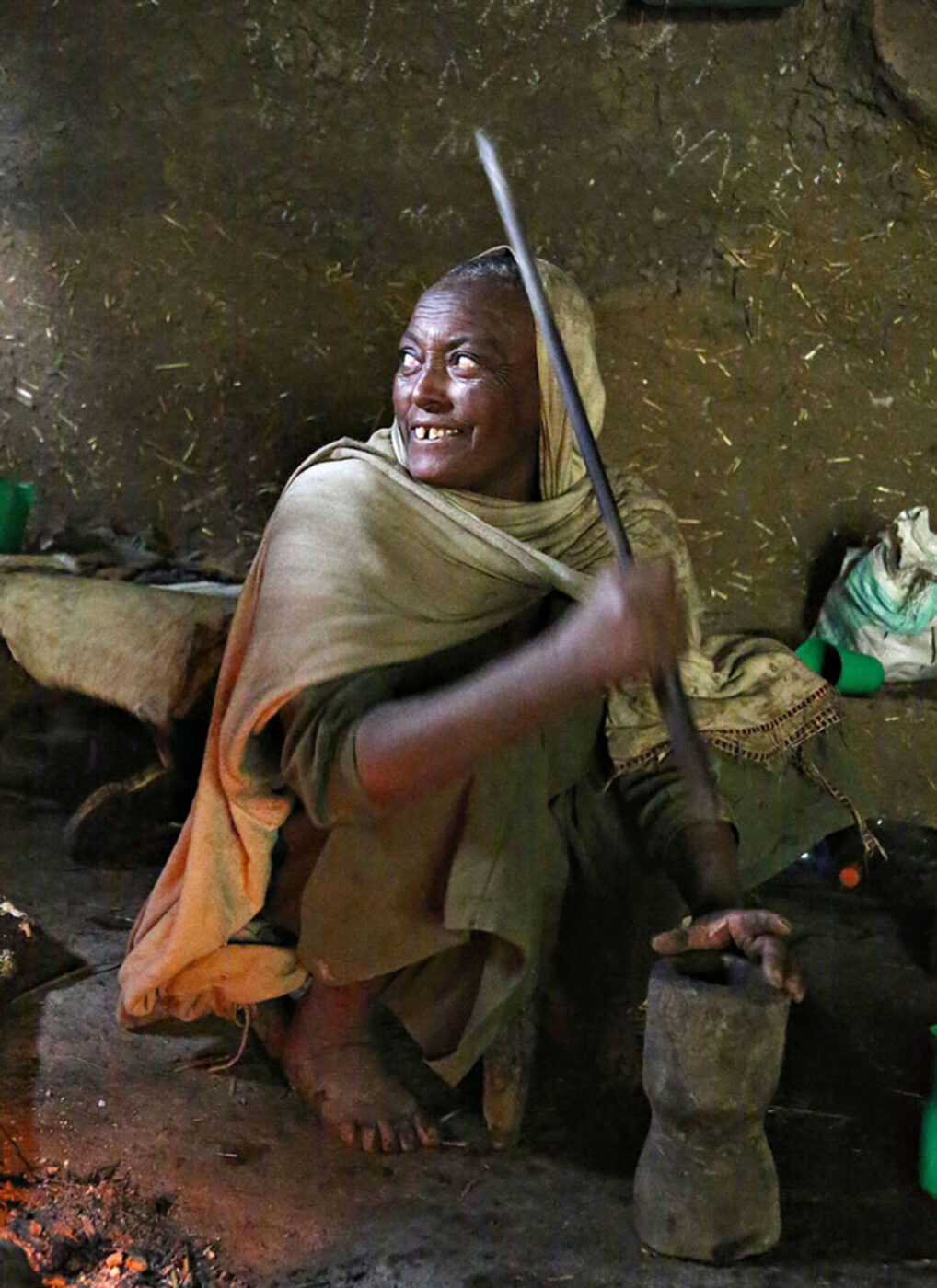 A woman using a long stick to grind coffee beans.