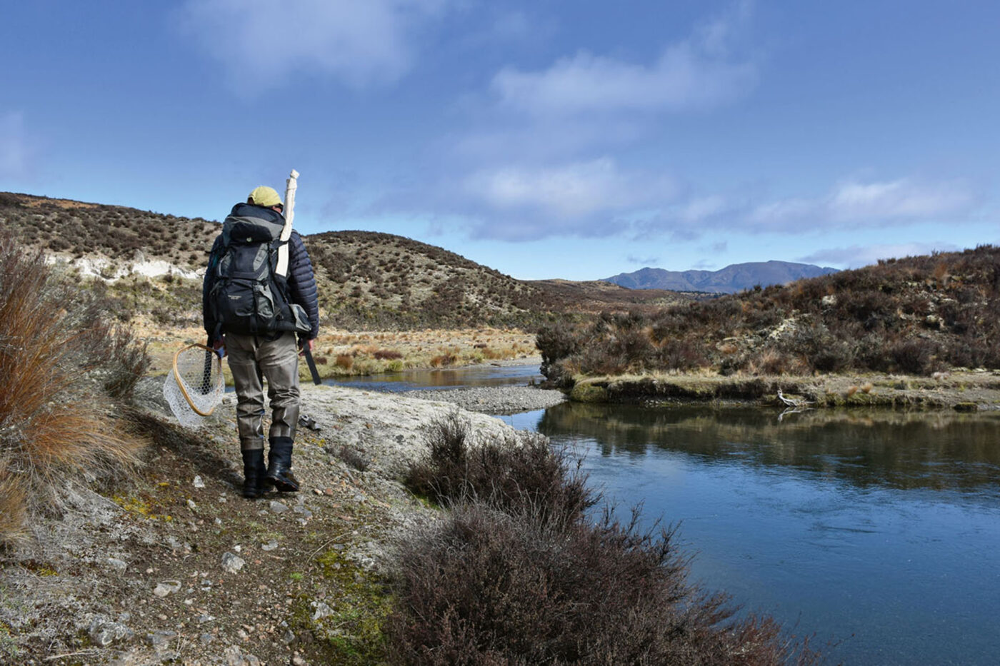 A fisherman standing next to a big lake, holding a net.