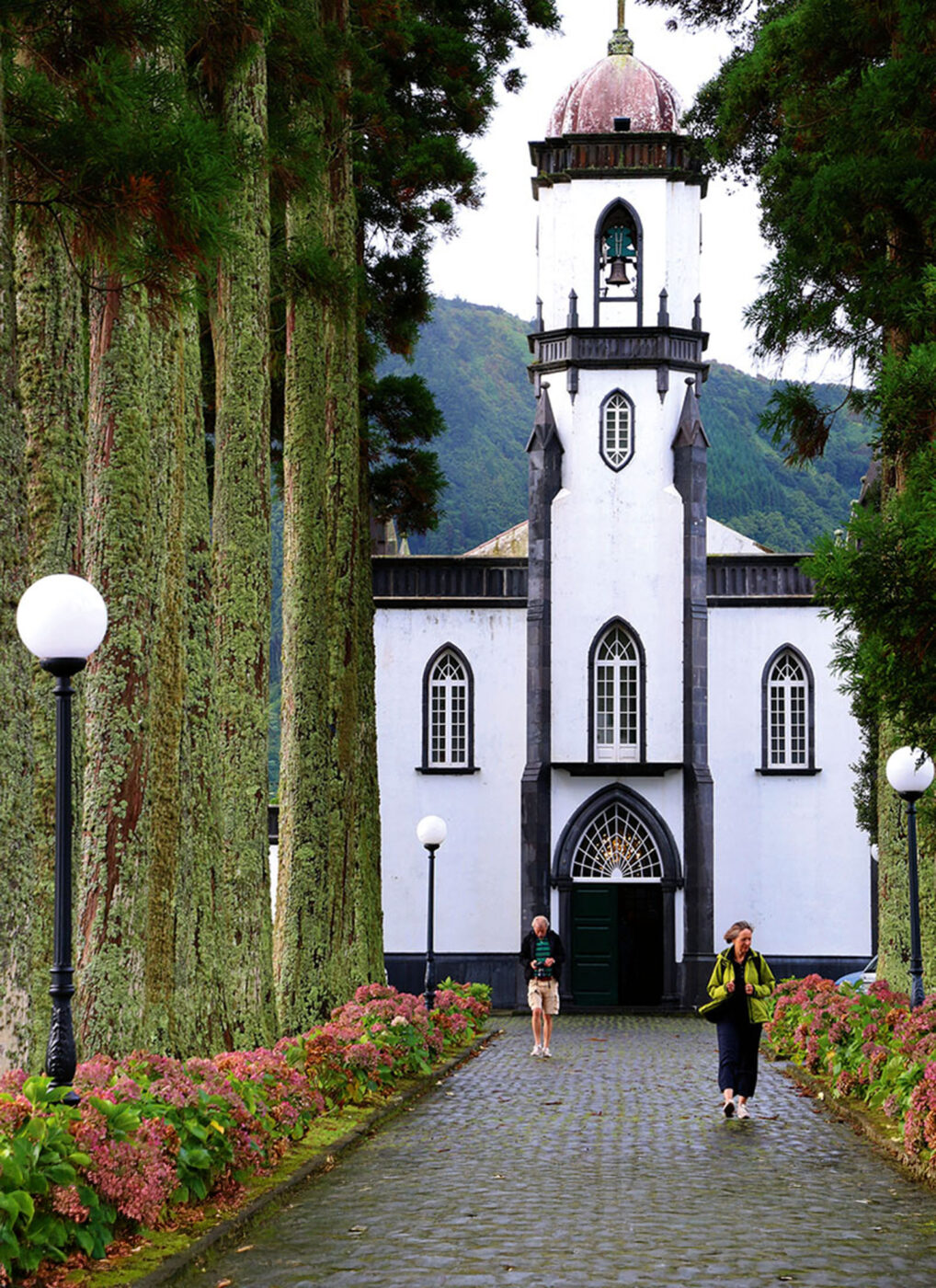A black and white church with people walking the path away from it.