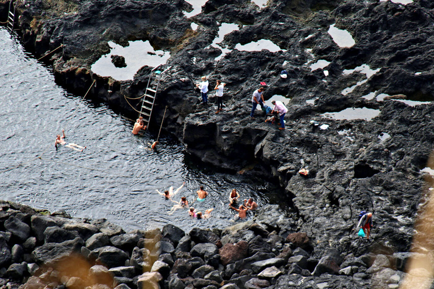 People swimming in a big body of mineral water, surrounded by rock pools.