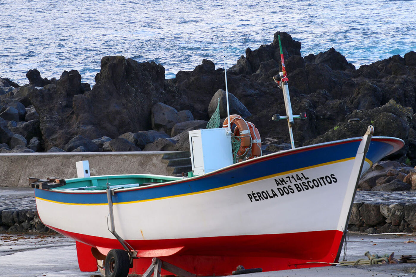 A small fishing boat hauled ashore in front of some rocks and the ocean.