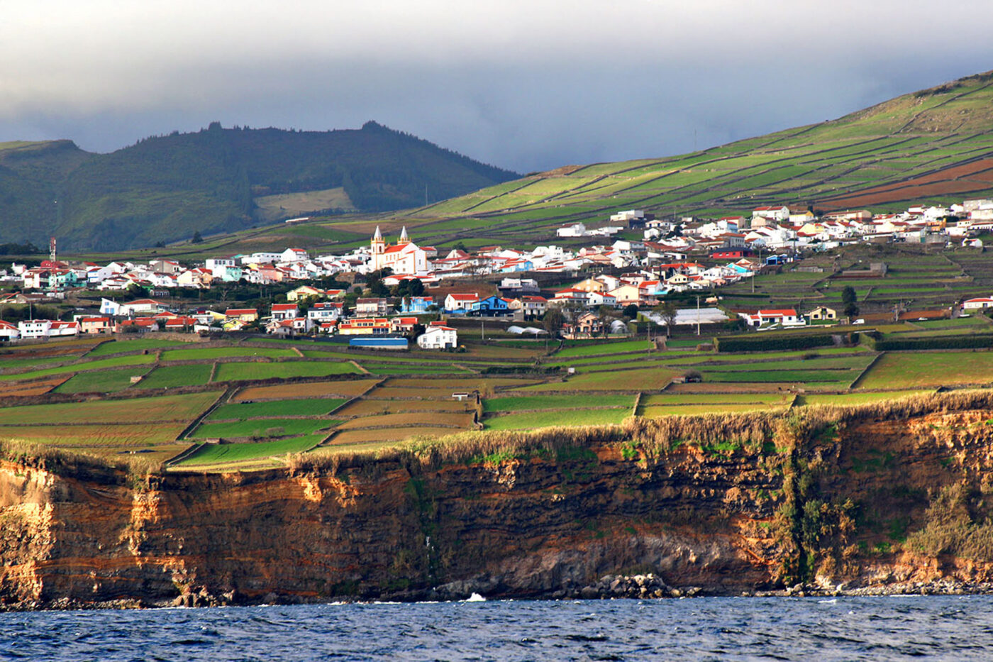A landscape shot of a small town on the side of a cliff. Taken from the sea.