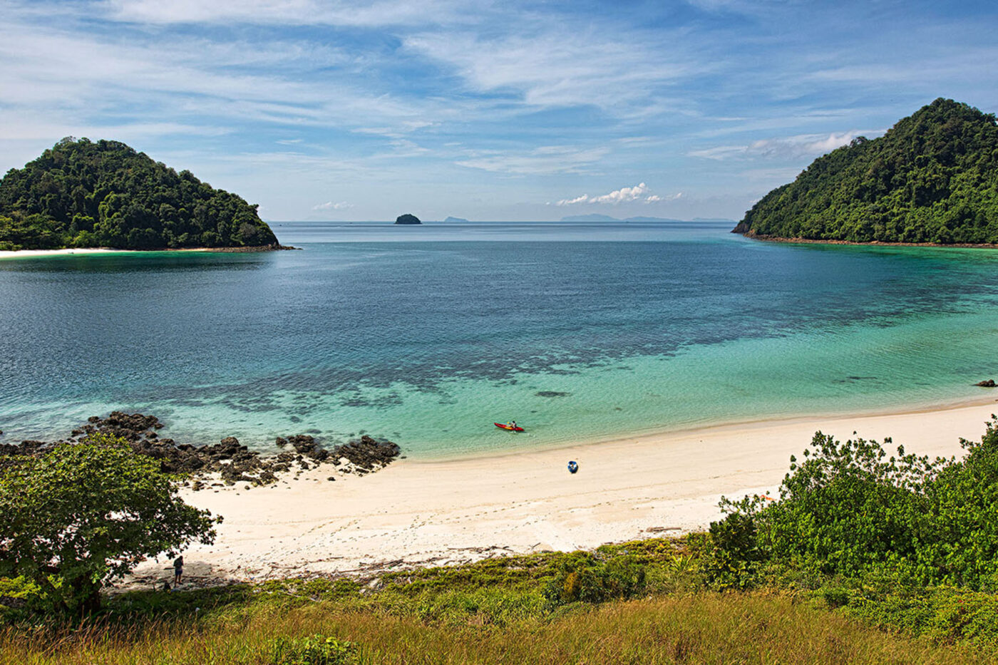 A big landscape shot of a beach, with one lonely person in a kayak close to the sand.