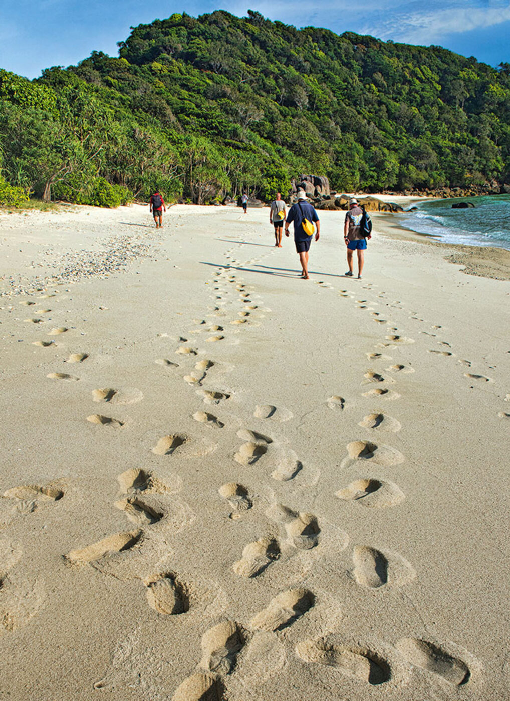 A group of people walking on the beach, footsteps in the stand trailing behind them.