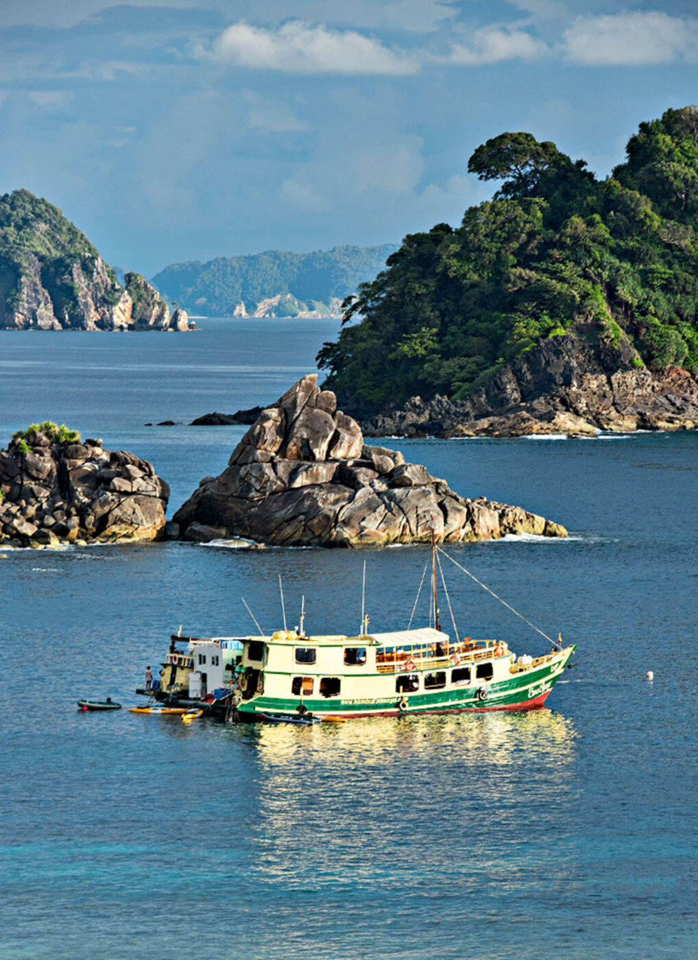 A shabby green and white boat floating on the water.
