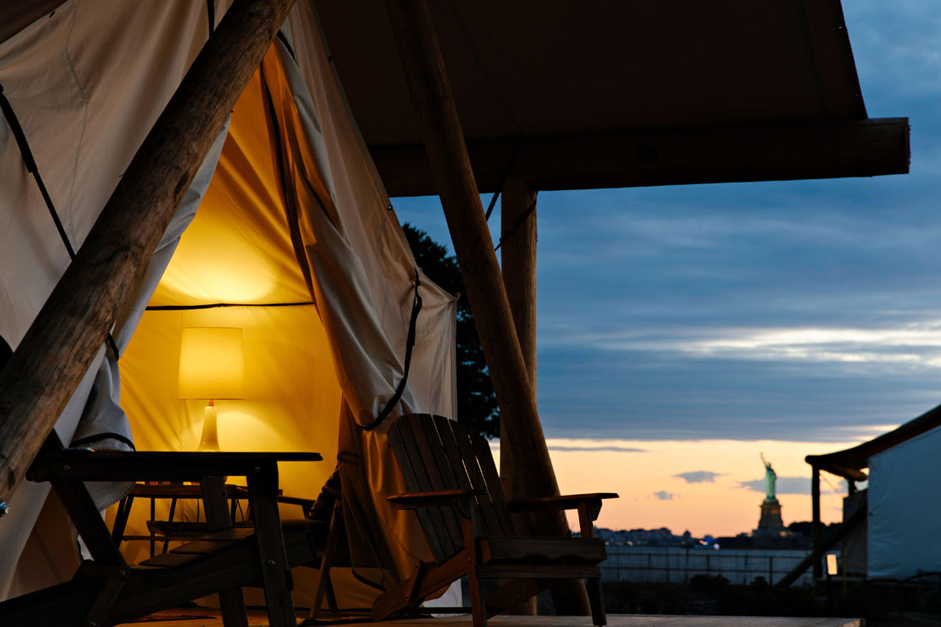 The side view of a big tent with a lamp inside. Outside, you can see the Statue of Liberty in the background.