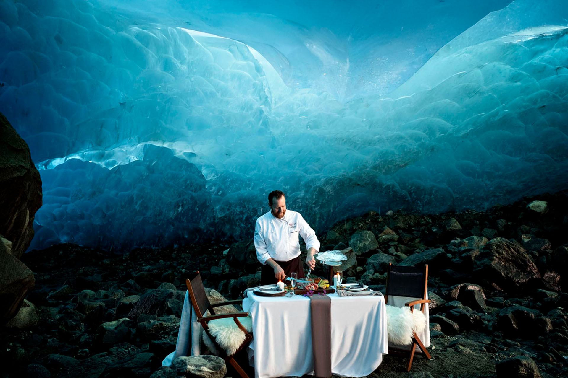A chef preparing food at a table in the middle of a blue ice cave.