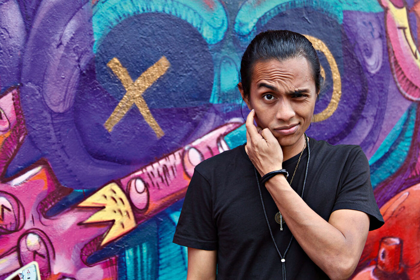 A person standing in front of Graffiti art with their hand on their cheek.